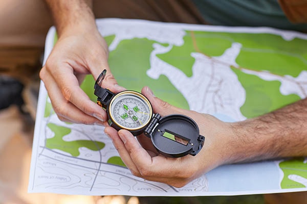 A hand holding a compass over a map.