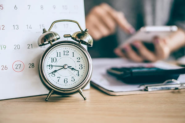 An alarm clock in front of a calendar. 