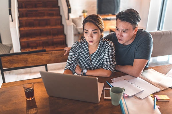 A couple looking at a laptop in their home discussing something with papers on the counter.