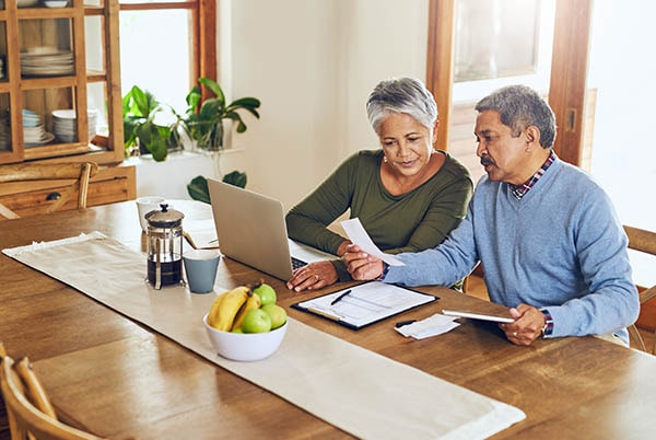 An older couple in their home looking at receipts with a laptop and tablet.