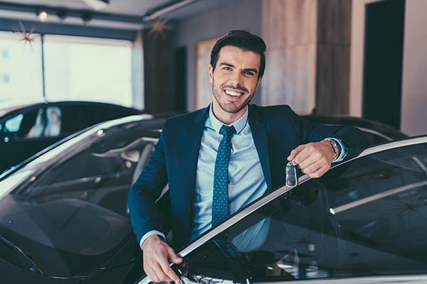 A young looking professional holding a key to a new car standing in the cars doorway.